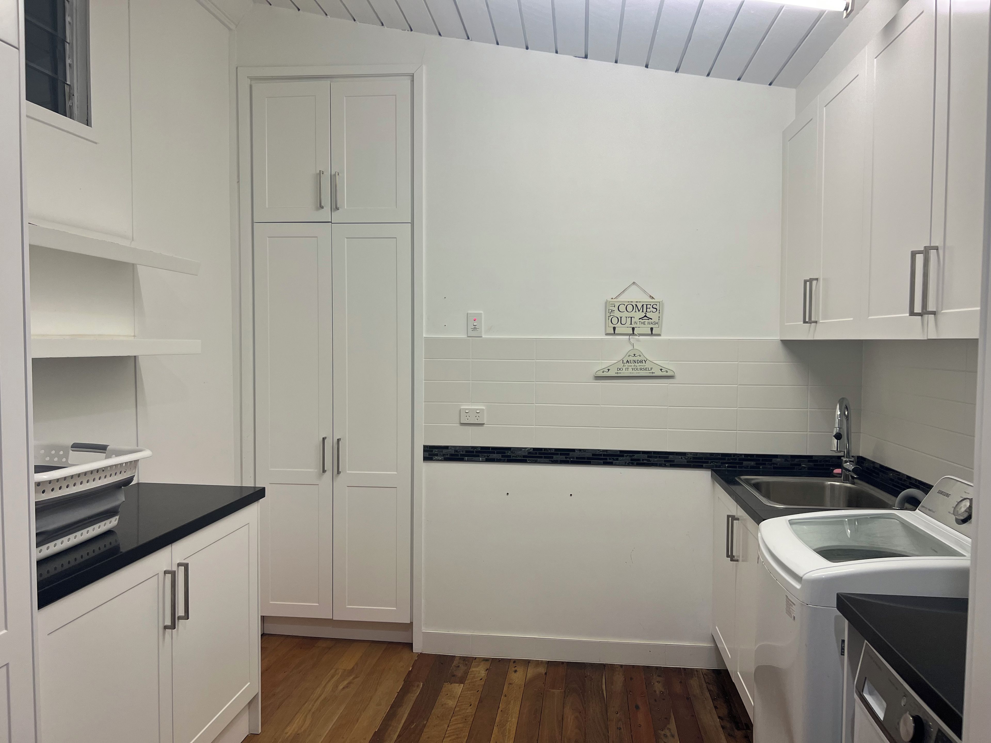 A compact kitchen with white cabinets, a black countertop, and a built-in washing machine.
