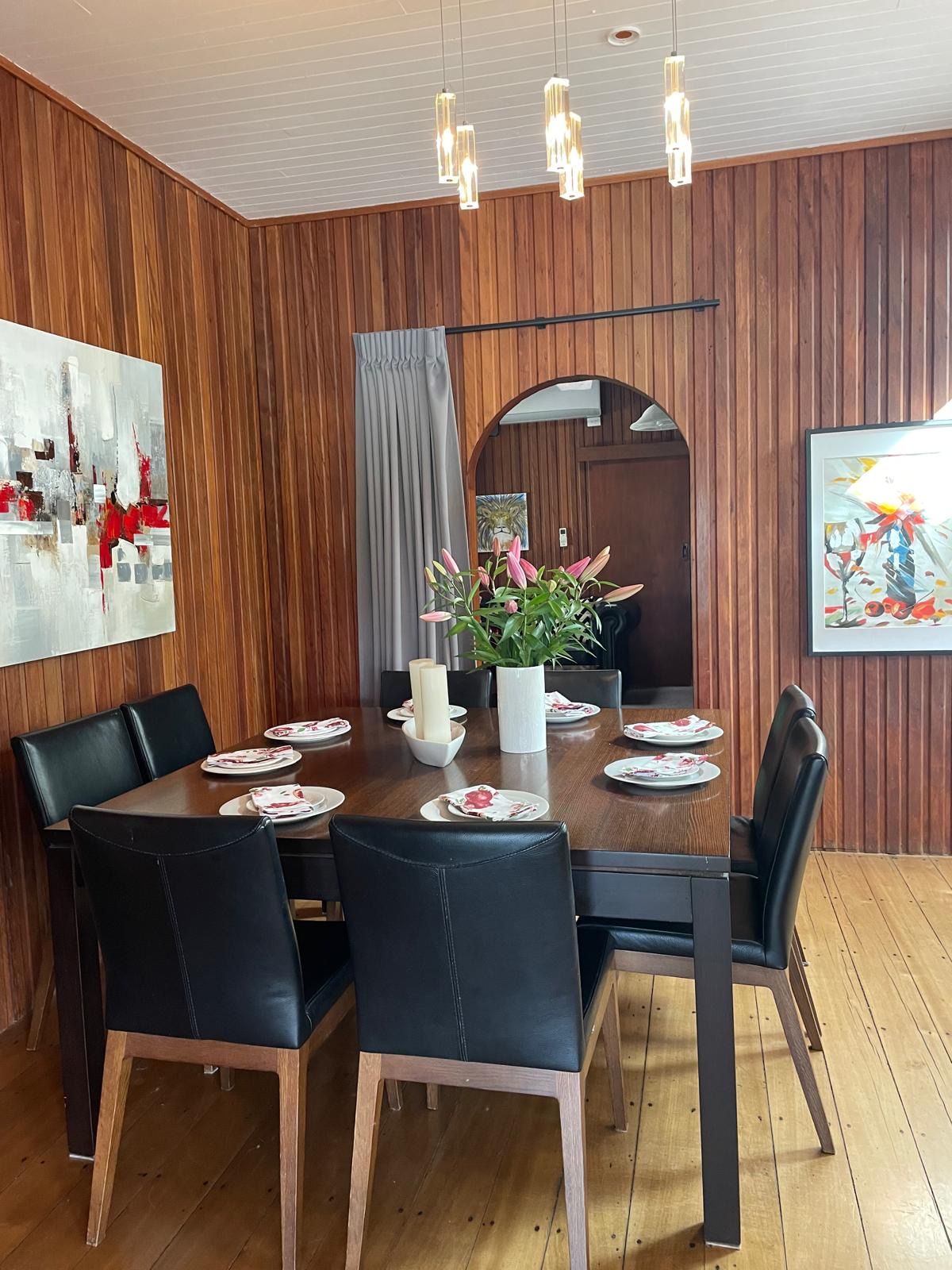 A dining area with a wooden table, black chairs, and a vase with flowers.