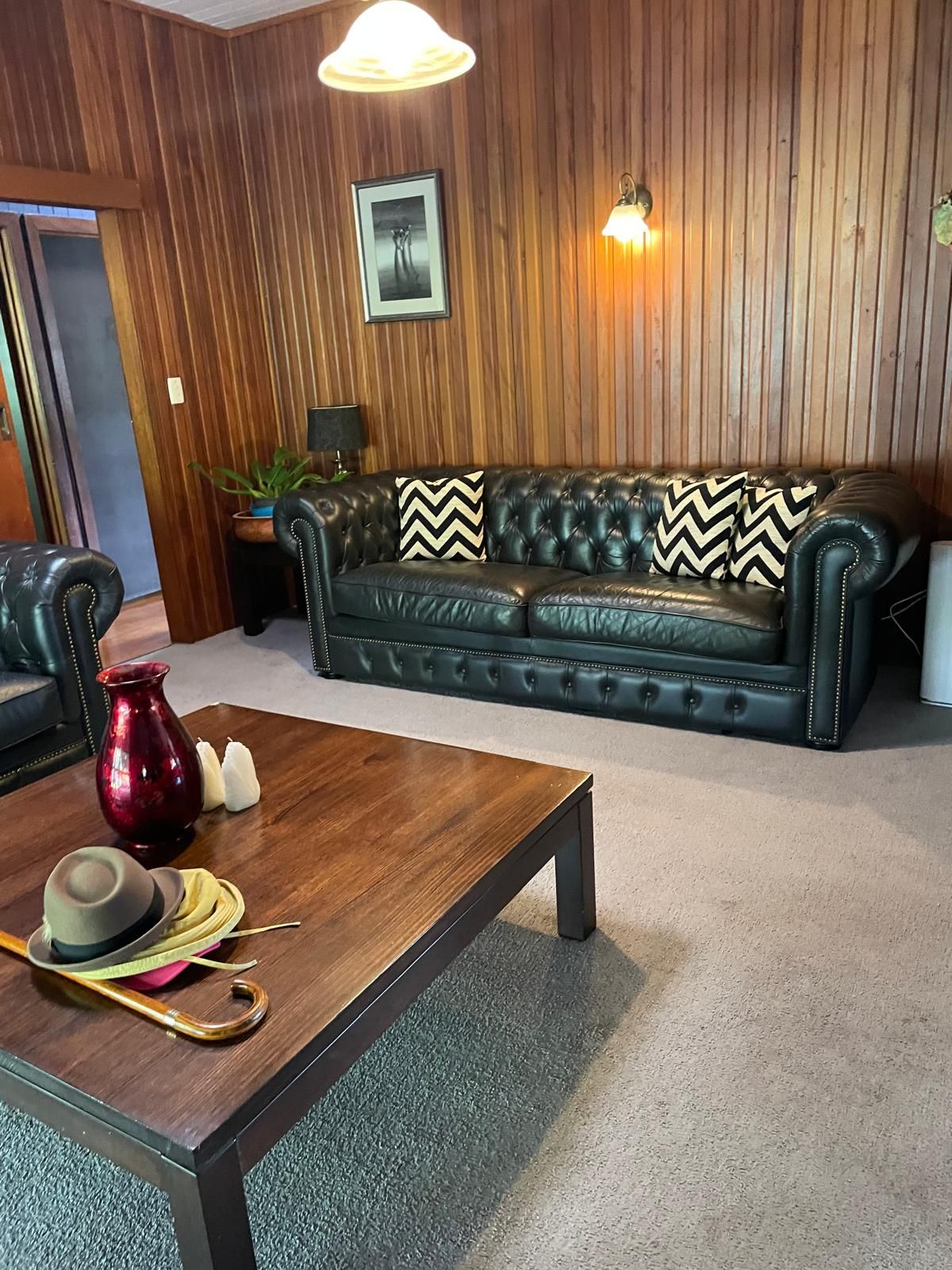 A room with a dark leather sofa, a wooden coffee table, and a red vase.