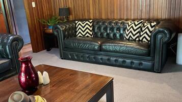A room with a dark leather sofa, a wooden coffee table, and a red vase.