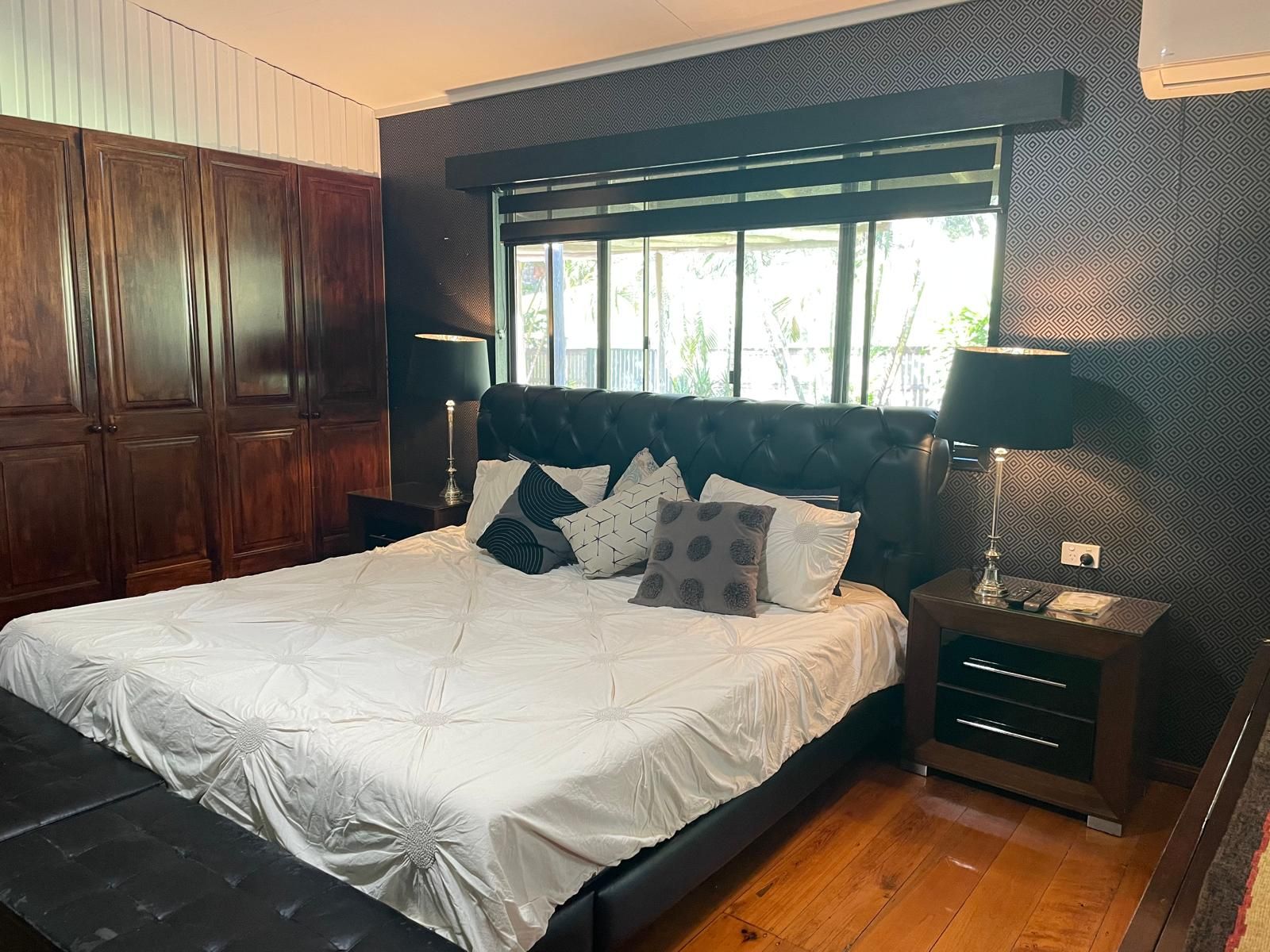 A bedroom with a large bed, wooden wardrobe, and a window with blinds.