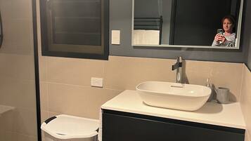 Une salle de bain avec un lavabo blanc, des meubles de rangement de couleur foncée et un miroir au-dessus.