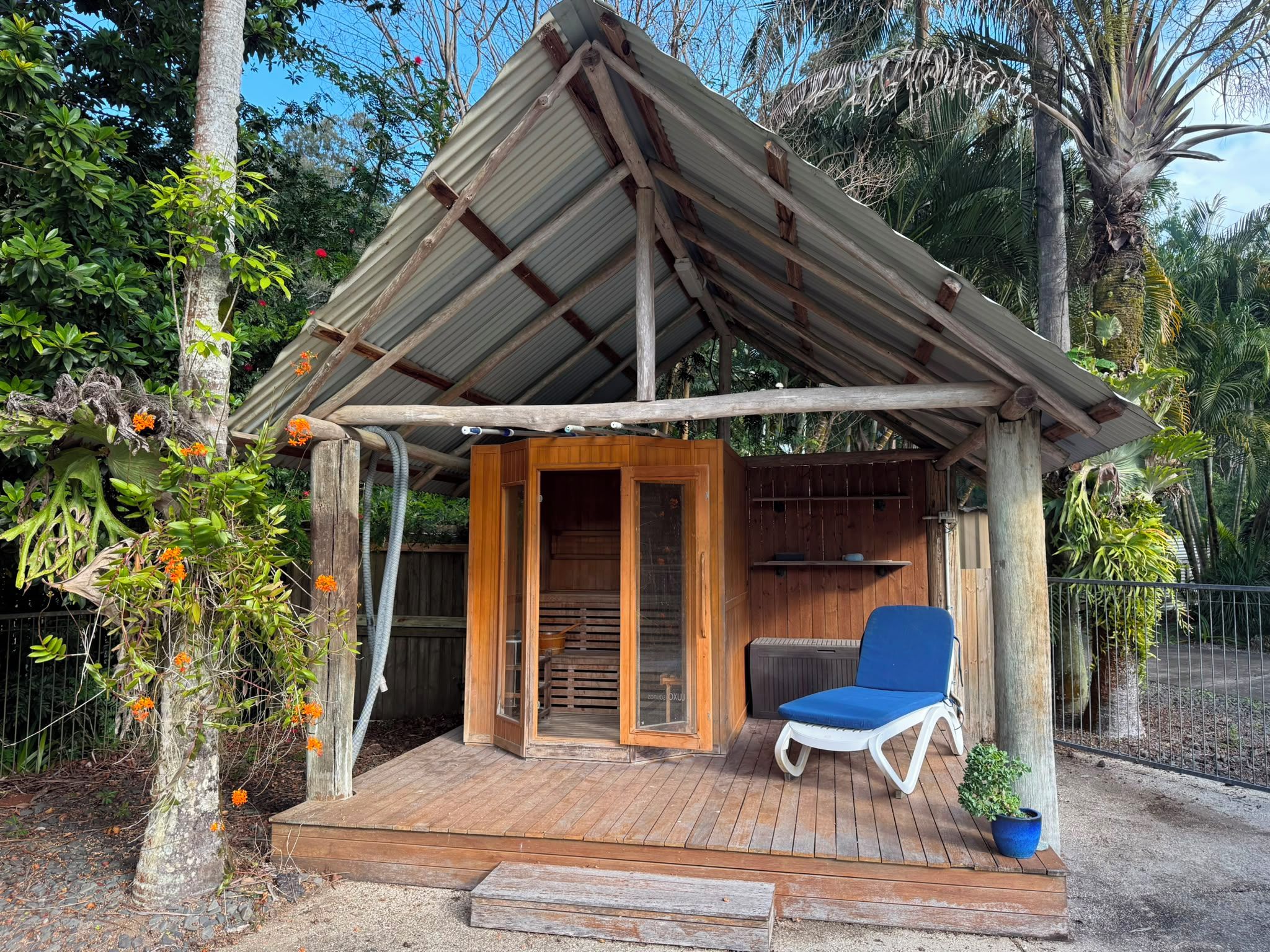 A wooden structure with a metal roof, a wooden deck, and a blue lounge chair.