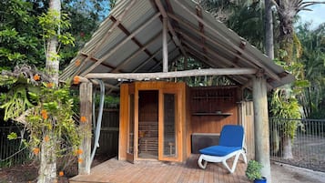 A wooden structure with a metal roof, a wooden deck, and a blue lounge chair.