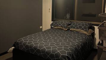 A bedroom with a bed, a ceiling fan, an air conditioning unit, a window, and a nightstand.