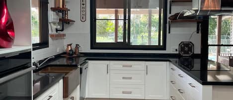 A modern kitchen with white cabinetry, a black countertop, and a wooden floor.