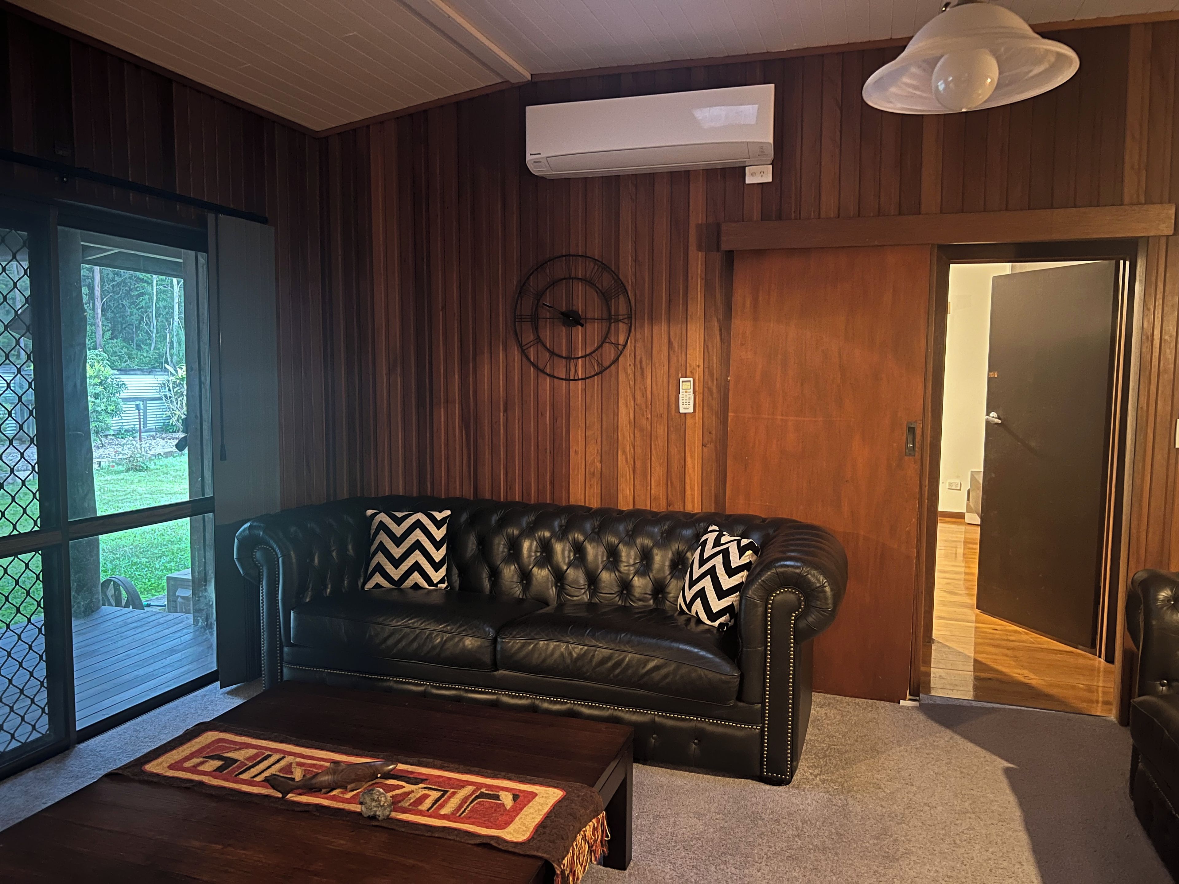Una habitación con sofá de cuero, pared de madera, equipo de aire acondicionado y una puerta.