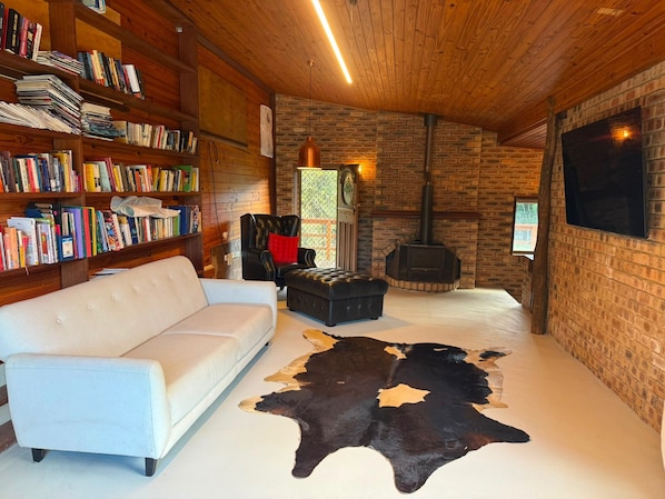 A cozy living room with a white sofa, leather ottoman, a large leather rug, a fireplace, and a bookshelf filled with books.