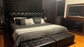 Une chambre à coucher avec un grand lit, une tête de lit, une table de chevet, une lampe, une commode et un téléviseur.