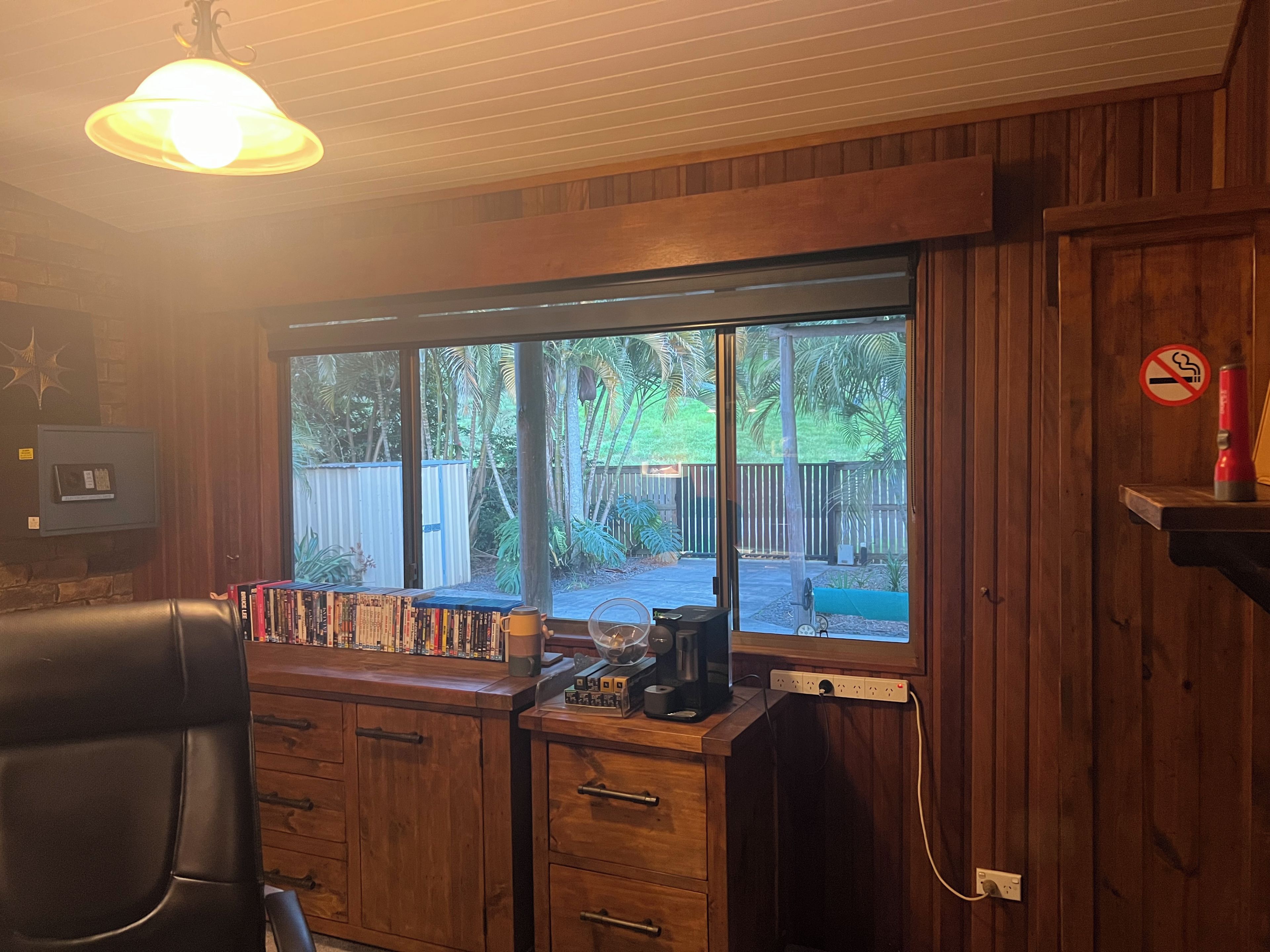 Une pièce avec un bureau en bois, une bibliothèque, une machine à café et une fenêtre donnant sur une courClose.