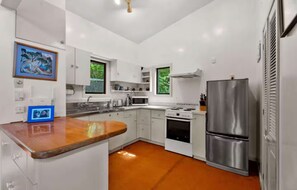 Una cucina moderna con mobili bianchi, un piano di lavoro in legno, elettrodomestici in acciaio inossidabile e vista su spazi verdi.