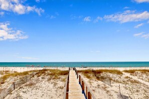 Une promenade en bois menant à une plage, avec un ciel dégagé.