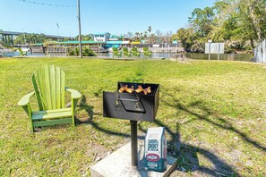 A barbecue grill with chicken, a green Adirondack chair, and a bag of Kingsford charcoal. - Summersalt Retreat• Canal Views • Walk to Dining • Pet Friendly (Gulf Shores)