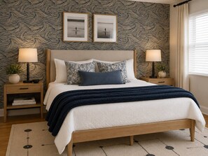 A bed with a wooden frame, two bedside tables, a patterned wallpaper, and two framed pictures on the wall. - Summersalt Retreat• Canal Views • Walk to Dining • Pet Friendly (Gulf Shores)