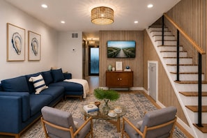 A modern living room with a sofa, armchairs, a coffee table, and a TV. - Summersalt Retreat• Canal Views • Walk to Dining • Pet Friendly (Gulf Shores)