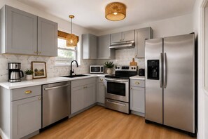A modern kitchen with grey cabinets, stainless steel appliances, a black faucet, and a wooden floor. - Summersalt Retreat• Canal Views • Walk to Dining • Pet Friendly (Gulf Shores)
