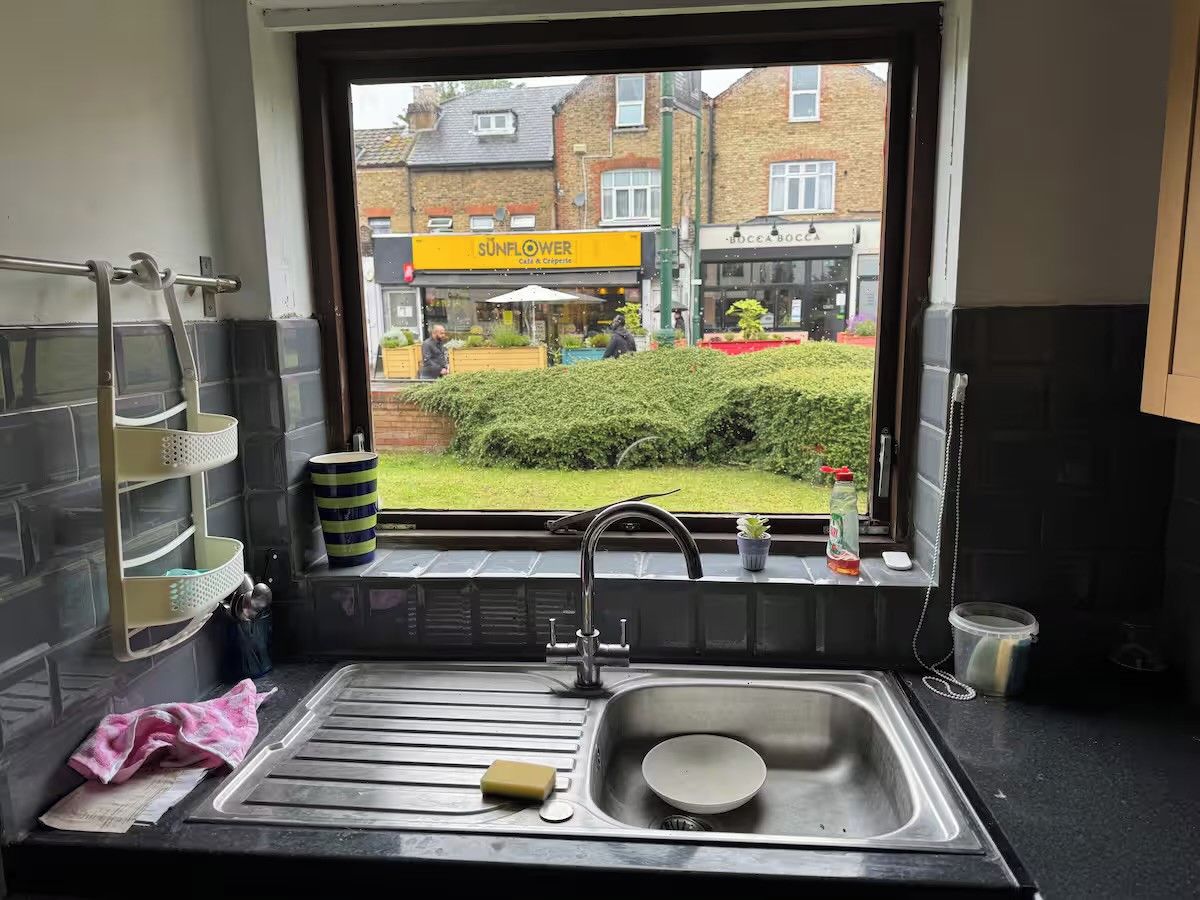 A kitchen with a stainless steel sink, a window with a view of a street, and a small potted plant on the windowsill.
