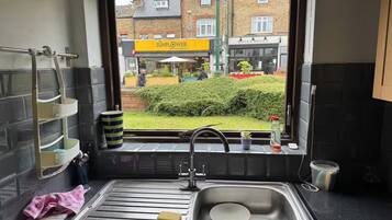 A kitchen with a stainless steel sink, a window with a view of a street, and a small potted plant on the windowsill.