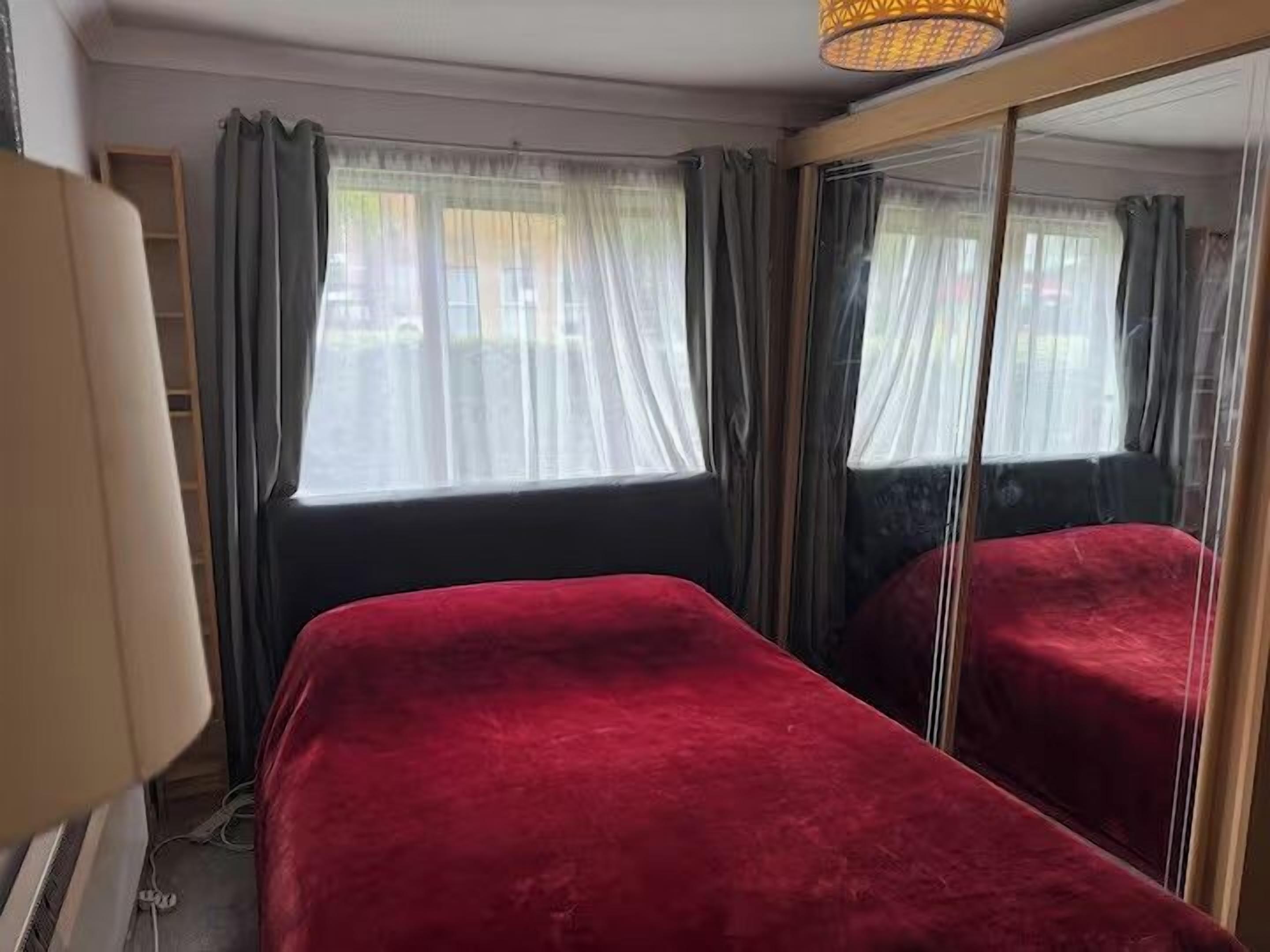 A room with a bed, a mirror, and a window with curtains.
