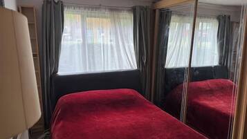 A room with a bed, a mirror, and a window with curtains.