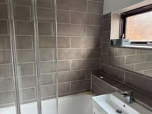A bathroom with a glass shower enclosure, a bathtub, and a sink with a window above. - Apartment Sleeps 4 with Parking (London)