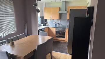 A modern kitchen with a dining area, featuring a wooden table and chairs, a black refrigerator, and wooden cabinets.