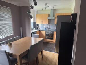 A modern kitchen with a dining area, featuring a wooden table and chairs, a black refrigerator, and wooden cabinets. - Apartment Sleeps 4 with Parking (London)