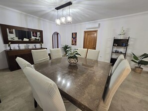 Een eetkamer met een grote rechthoekige tafel, witte fauteuils, een decoratieve schaal in het midden en een plafondlamp.