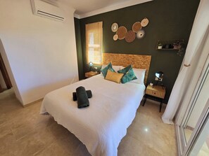 Een slaapkamer met een bed, een nachtkastje, een lamp, een raam met zonwering en wanddecoratie.