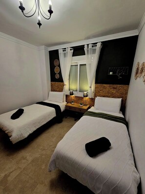Ein Hotelzimmer mit zwei Einzelbetten, einem kleinen Tisch mit Lampe, einem Fenster mit Vorhängen und einem Wandbild.