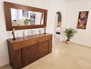 A wooden console with decorative items, a large mirror, and a potted plant in a hallway. - 3 Bed Apartment - Sleeps 6 - Pool - Parking - Golf (Mijas)