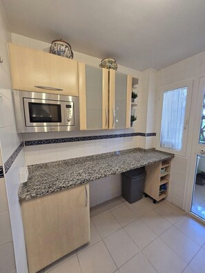 A kitchen with a microwave, cabinets, a granite countertop, and a trash bin. - 3 Bed Apartment - Sleeps 6 - Pool - Parking - Golf (Mijas)