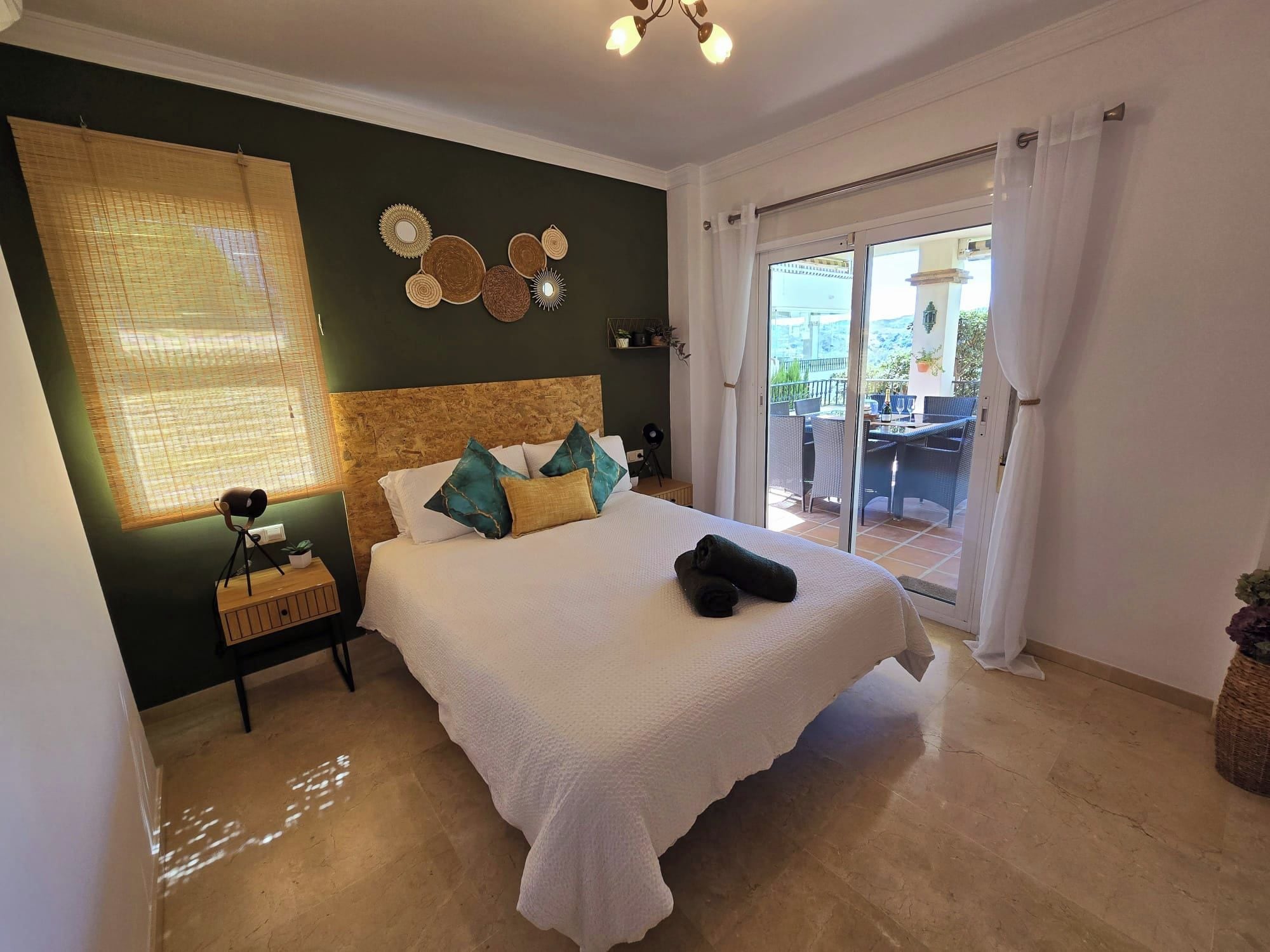 A bedroom with a large bed, a nightstand, a lamp, and a view of an outdoor balcony.