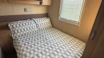 Une chambre compacte dans un véhicule récréatif, comprenant un lit, une fenêtre avec stores et des armoires intégrées en bois.