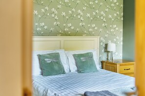 A bed with a checkered bedspread and two pillows, one with a dragonfly design, against a wall with a floral wallpaper pattern. - One Bed Bungalow Sleeps 4 - Garden - WiFi & Tv (Andover)