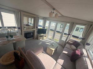 Ein geräumiger Wohnbereich mit einer Couch, Fernseher und einem Esstisch mit Untersetzern.