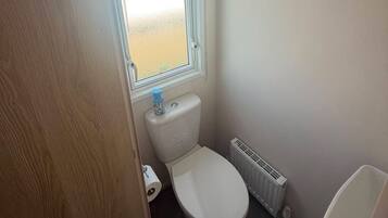 A small bathroom with a toilet, a radiator, and a window with a view of the beach.