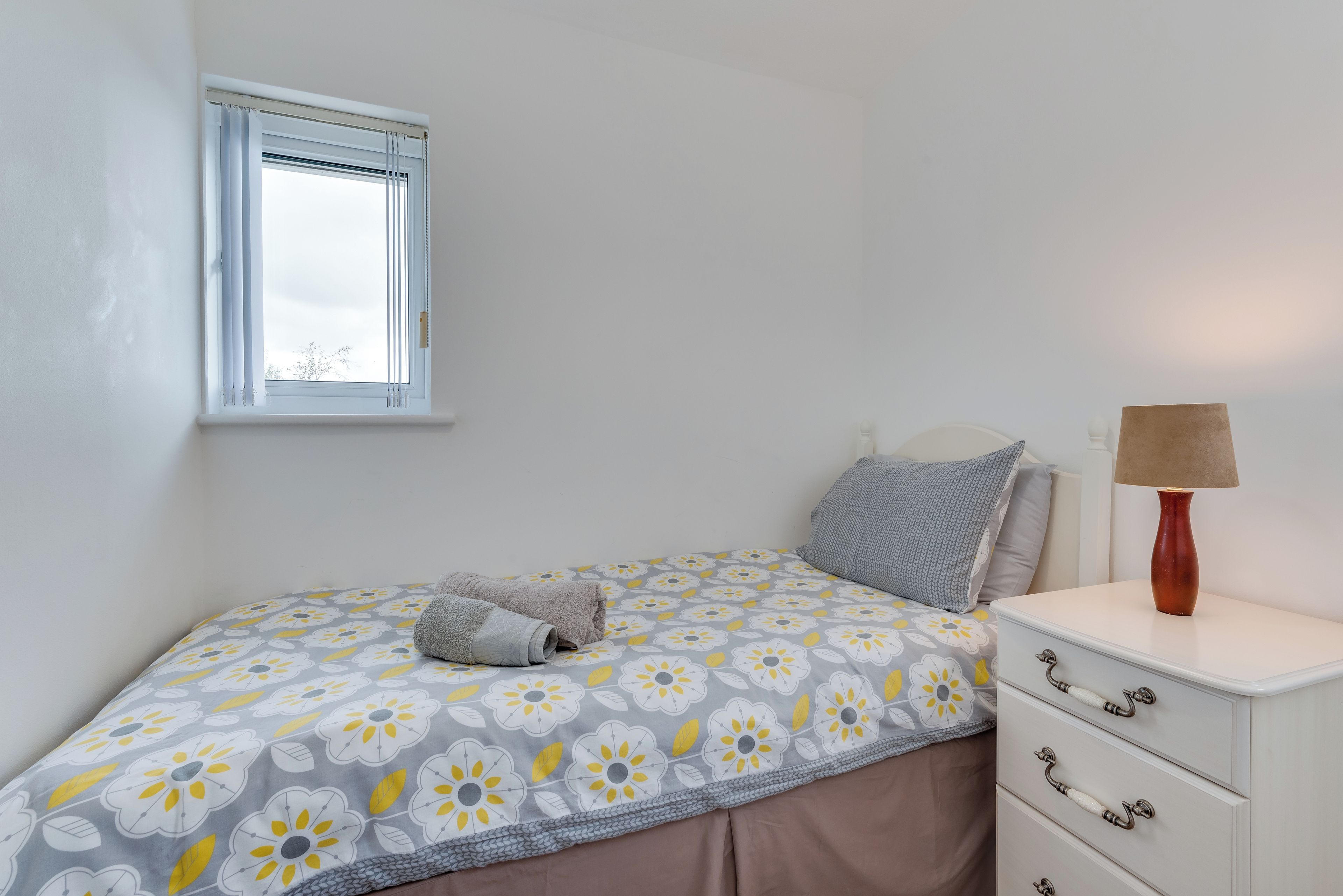 Une chambre à coucher avec un lit, une table de chevet, une lampe et une fenêtre.
