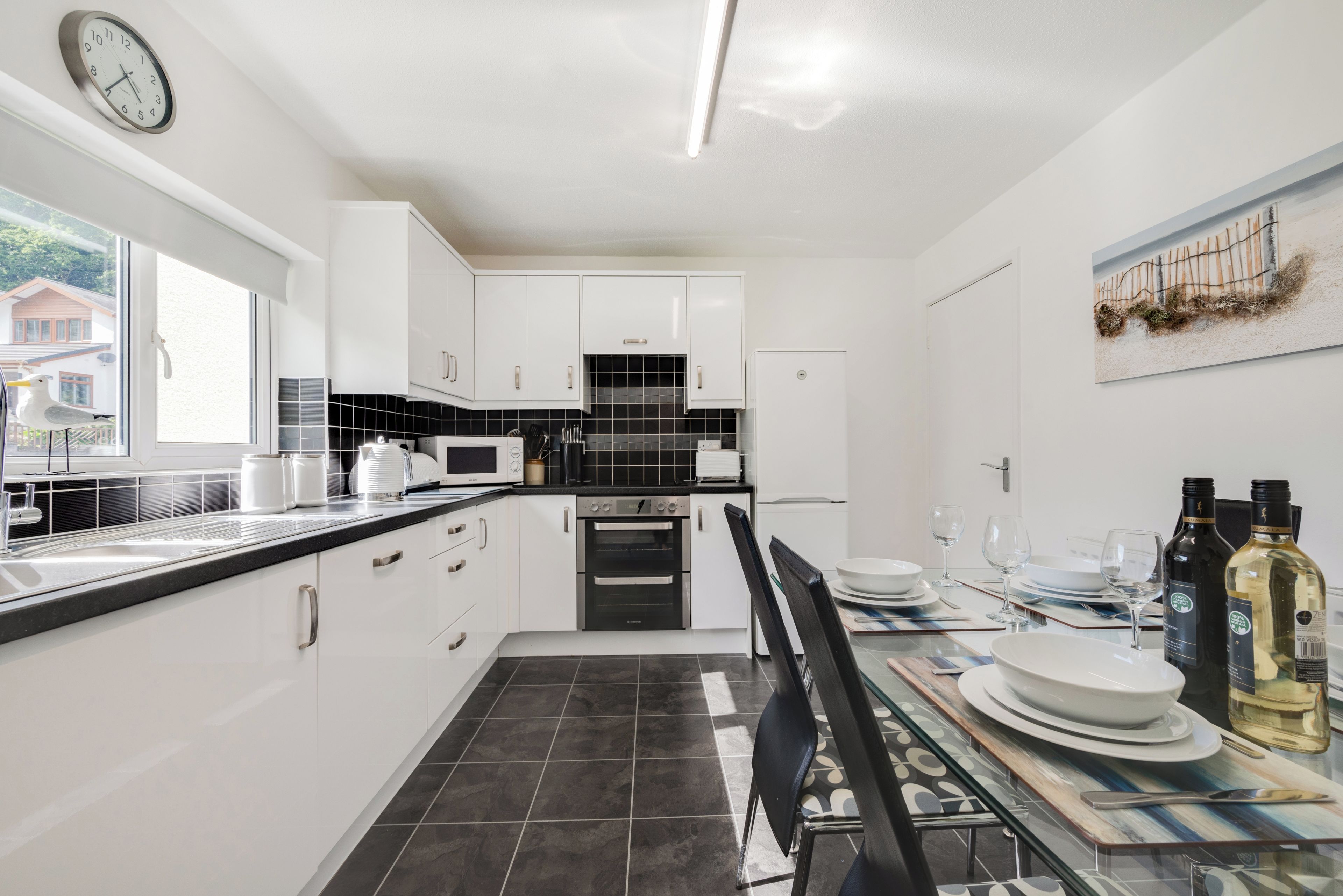 A modern kitchen with white cabinets, a black tiled backsplash, and a dining area with a table set for two.