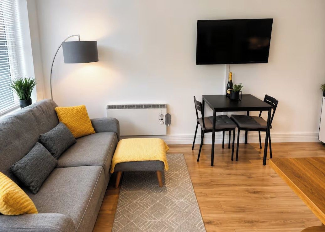Un salon moderne comprenant un canapé, une table basse, une table à manger avec des chaises, un téléviseur à écran plat fixé au mur et une lampe sur pied.