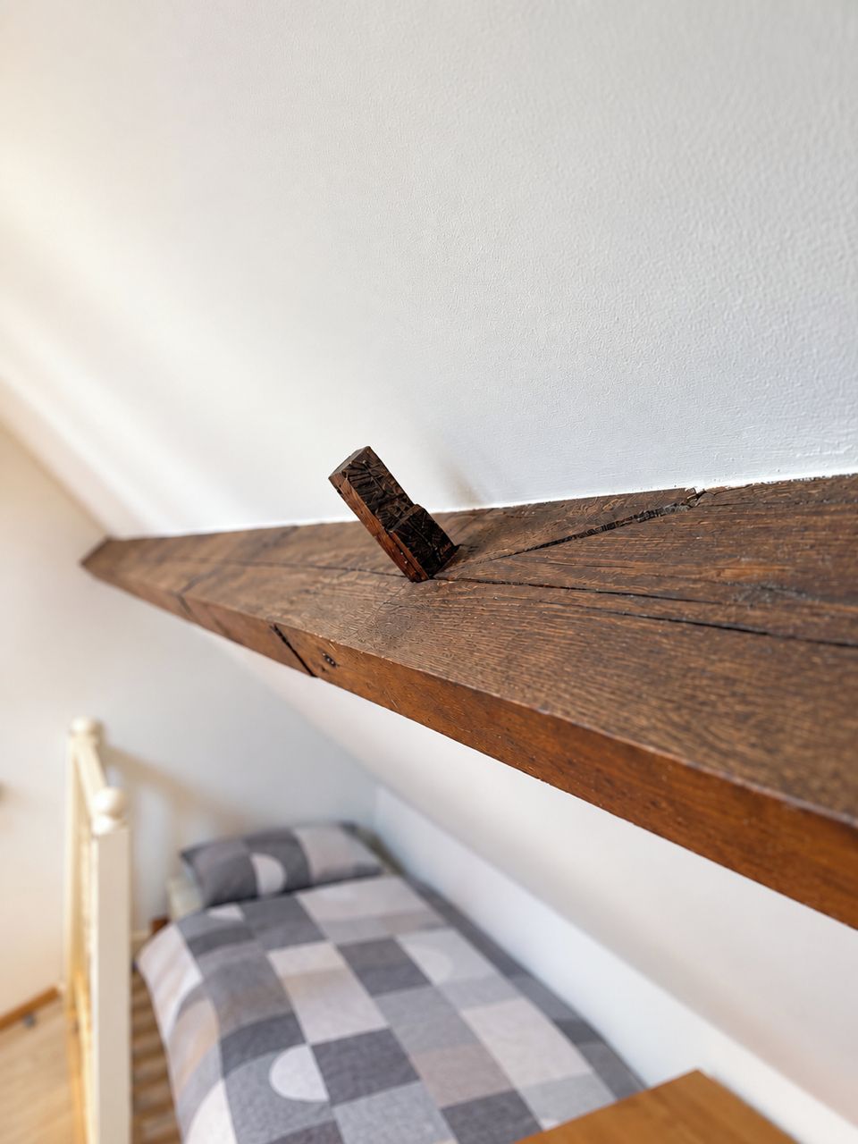 Un estante de madera con acabado rústico, un bloque de madera pequeño y un cojín a cuadros sobre una cama.