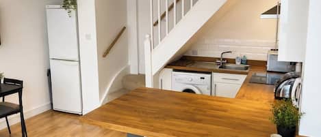 A modern kitchen with a wooden countertop, a built-in washing machine, and a staircase with white railings.