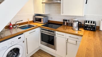A compact kitchen with a washing machine, microwave, toaster, and a wooden countertop.