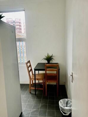 A small room with a table and two chairs, a potted plant, a tiled floor, and a window with a view of buildings. - Apartment Sleeps 4 near Station (London)