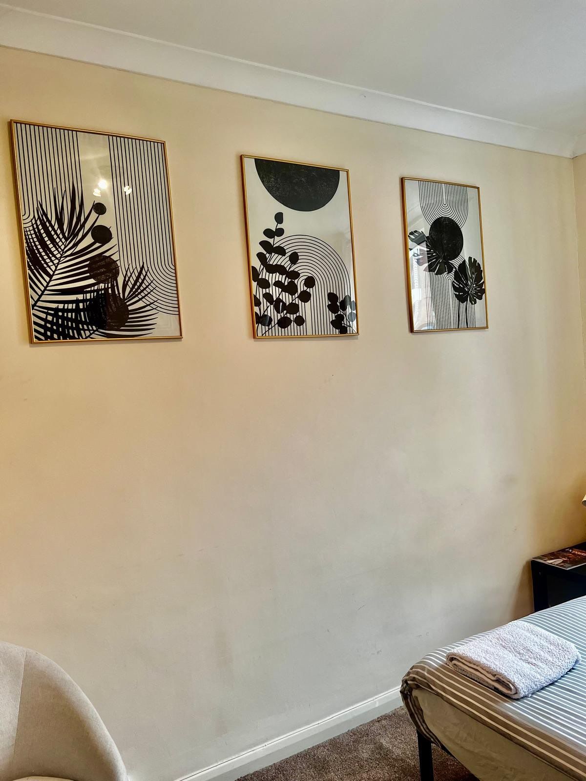 A room with a bed, a chair, and three wall-mounted artworks.
