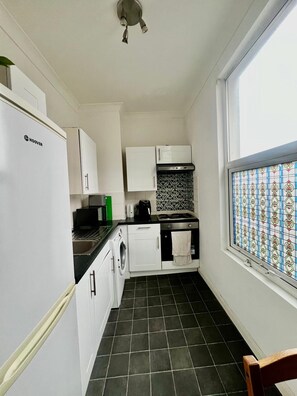 A compact kitchen with a refrigerator, stove, sink, and a washing machine. - Apartment Sleeps 4 near Station (London)