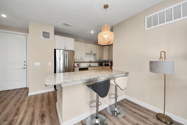 A modern kitchen with a central island, bar stools, a pendant light, and a floor lamp.