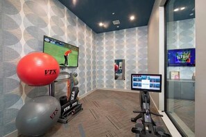 A fitness room with exercise equipment, a TV screen, and a digital kiosk.
