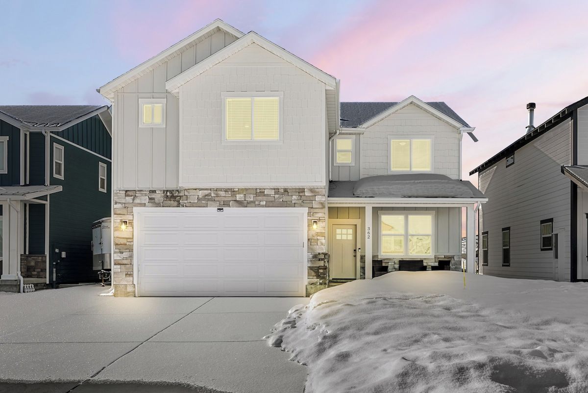 A two-story house with a garage, a driveway, and a snow-covered front yard.