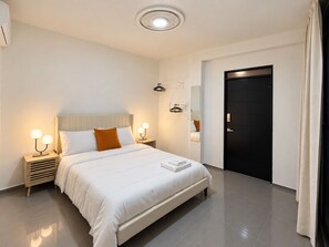 Ett modernt hotellrum med en stor säng, sängbord med lampor, en garderob och en dörr.